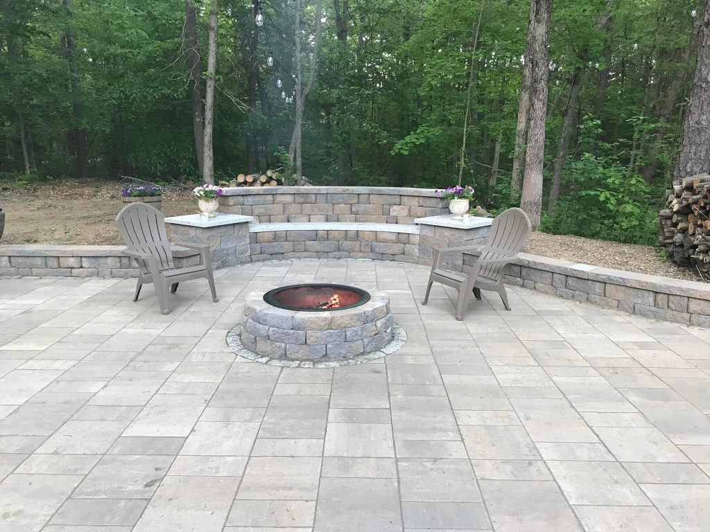 Round stone fire pit with a curved paver seat wall and Adirondack chairs on a paver patio