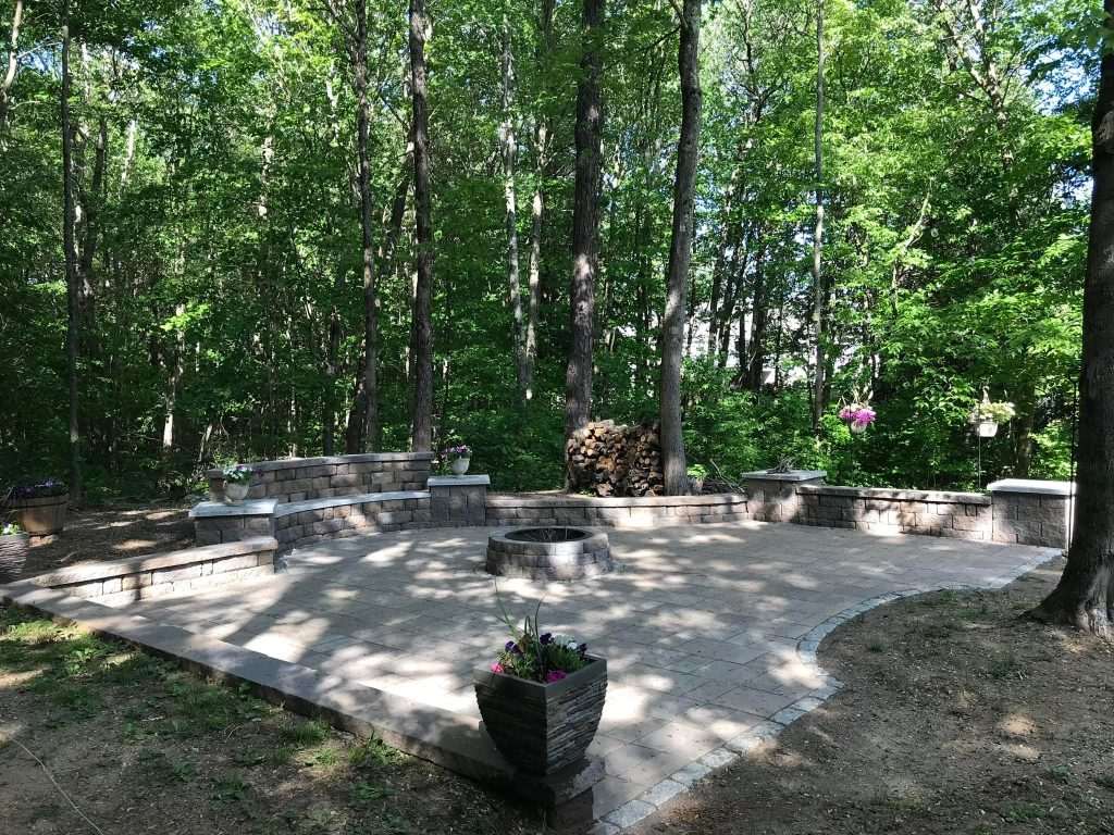 Curved paver patio with a low seat wall built into a wooded back yard