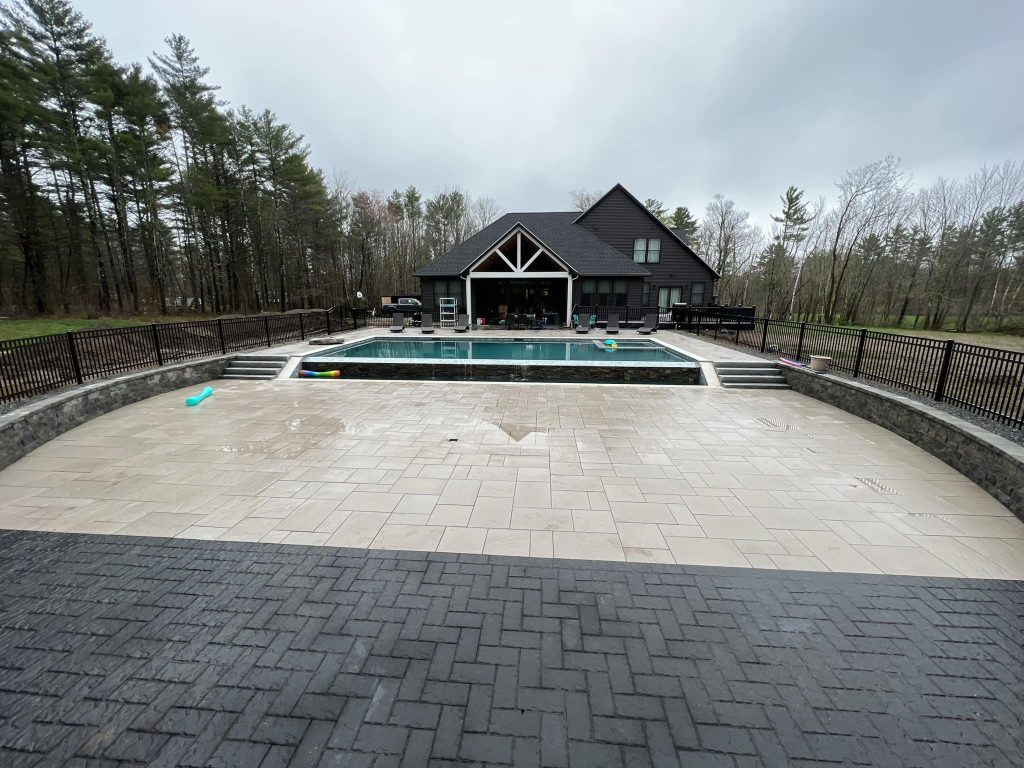 Paver pool deck surrounding an inground pool behind a large home